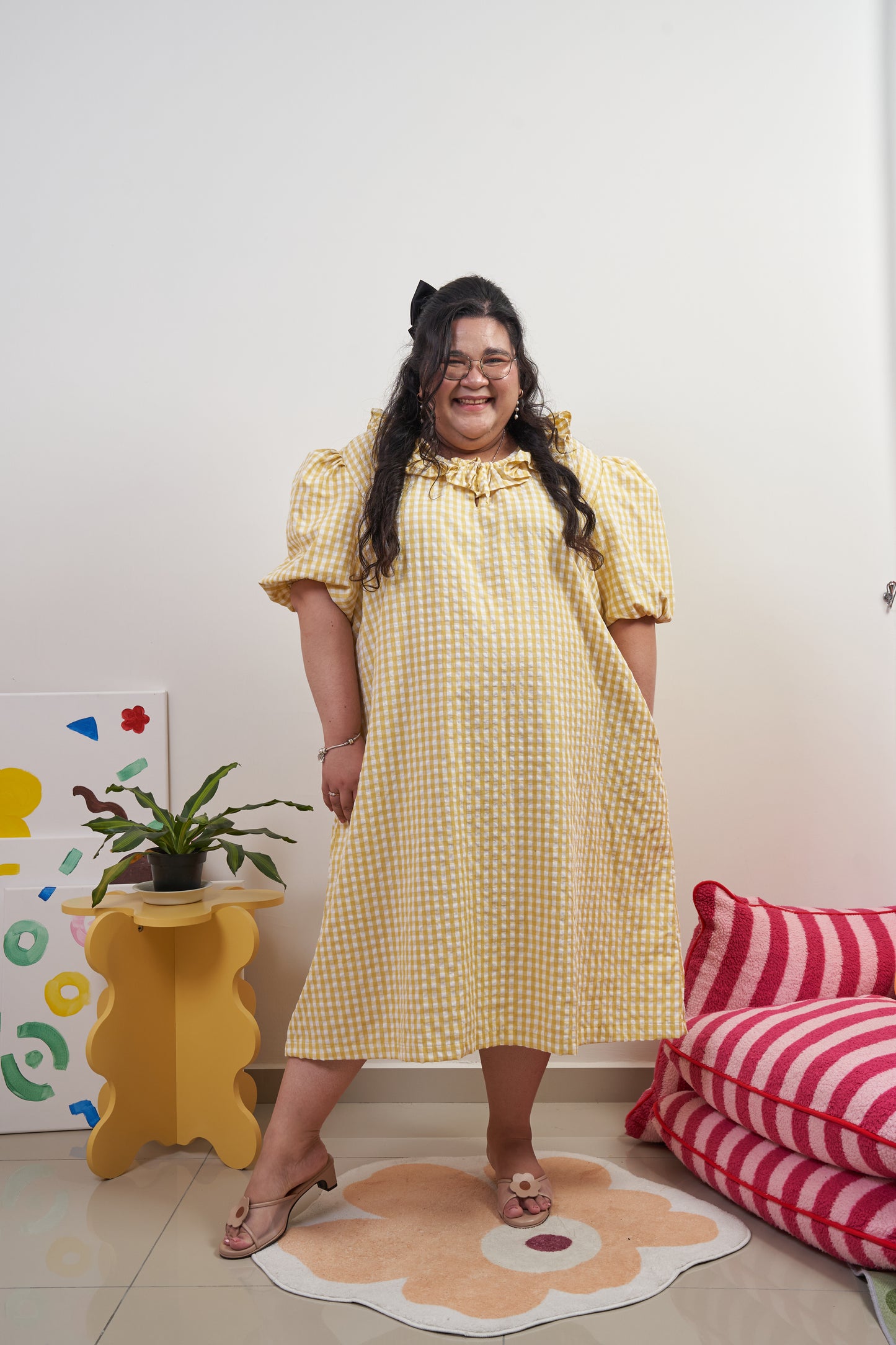 Full frontal view of Bea Dress in Sunny Gingham, model looking happy, featuring yellow gingham print, puffed sleeves, adjustable ruffled neckline, and relaxed trapeze silhouette