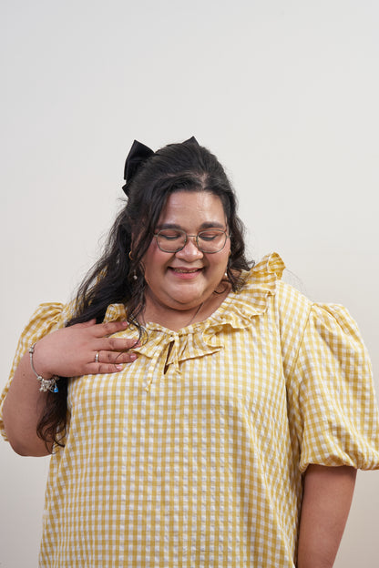 Close-up front view of Bea Dress in Sunny Gingham, showcasing adjustable ruffled neckline with yellow gingham print and puffed sleeves.