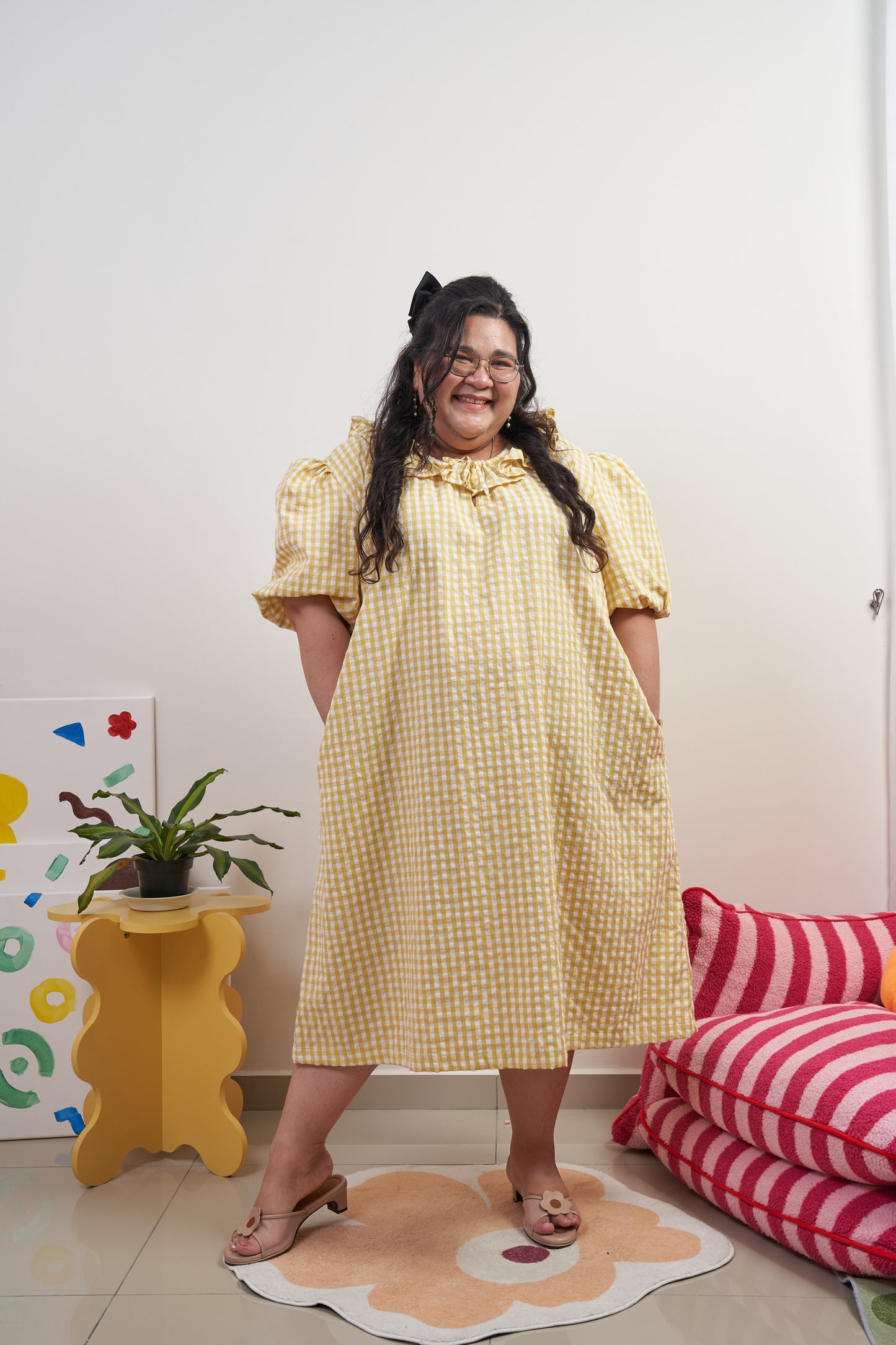 Full frontal view of Bea Dress in Sunny Gingham, model with both hands in pockets, featuring yellow gingham print, puffed sleeves, adjustable ruffled neckline, and relaxed trapeze silhouette.