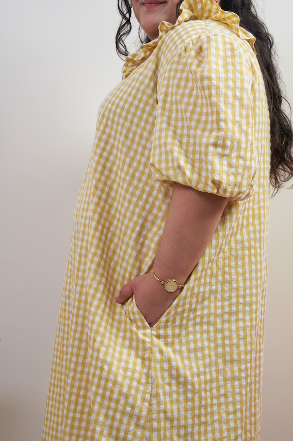 Semi-close-up side view of Bea Dress in Sunny Gingham, highlighting the side seam pocket with yellow gingham print and puffed sleeves