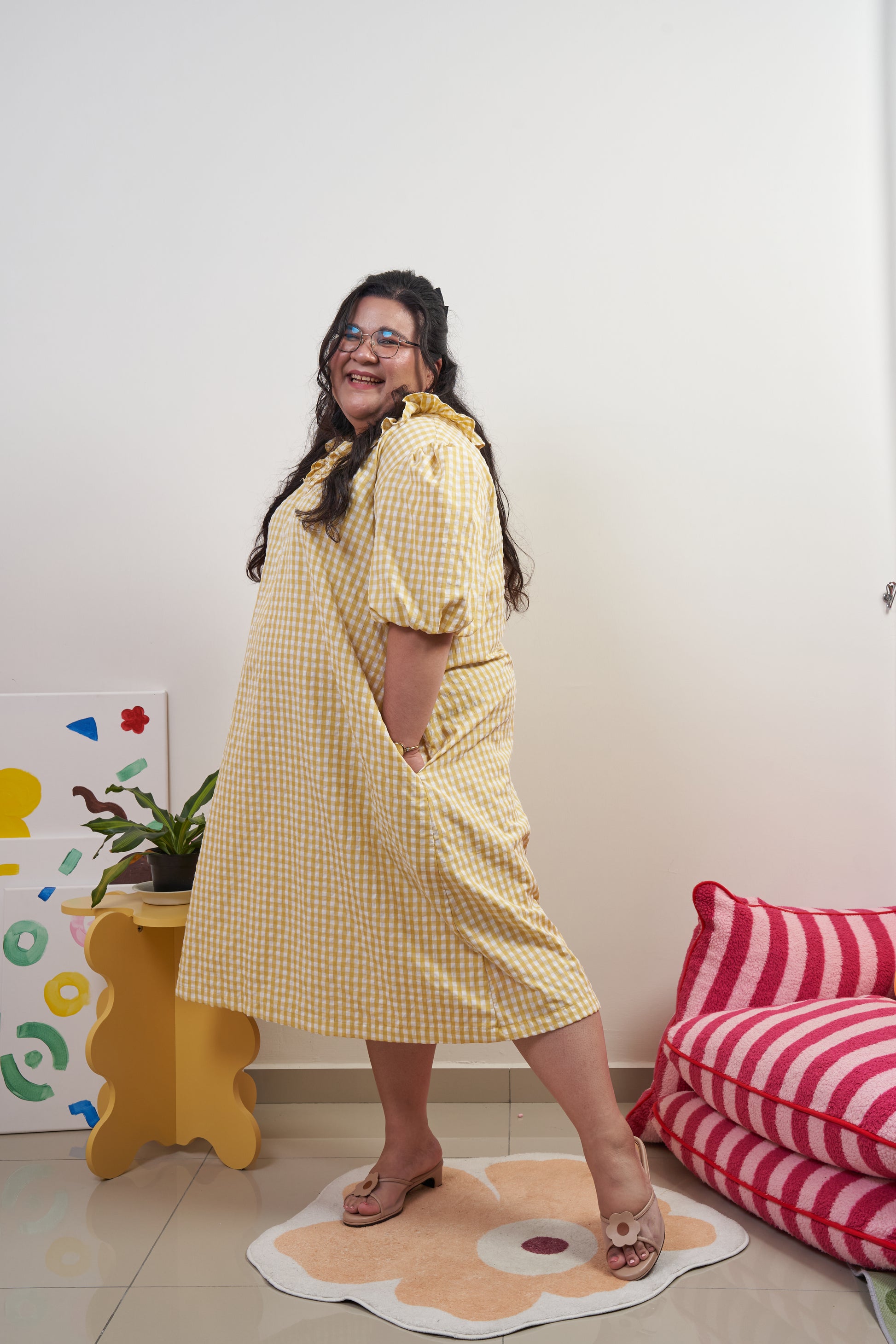 Side-profile view of Bea Dress in Sunny Gingham, model showing flowy movement with yellow gingham print, puffed sleeves, adjustable ruffled neckline, and relaxed trapeze silhouette