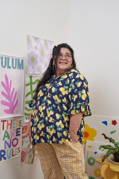 Front-side profile of Buttoned Belle Blouse in Lemon Dream, showing lemon print and ruffled sleeves, styled with Flutter Flair Pants in Lemonade