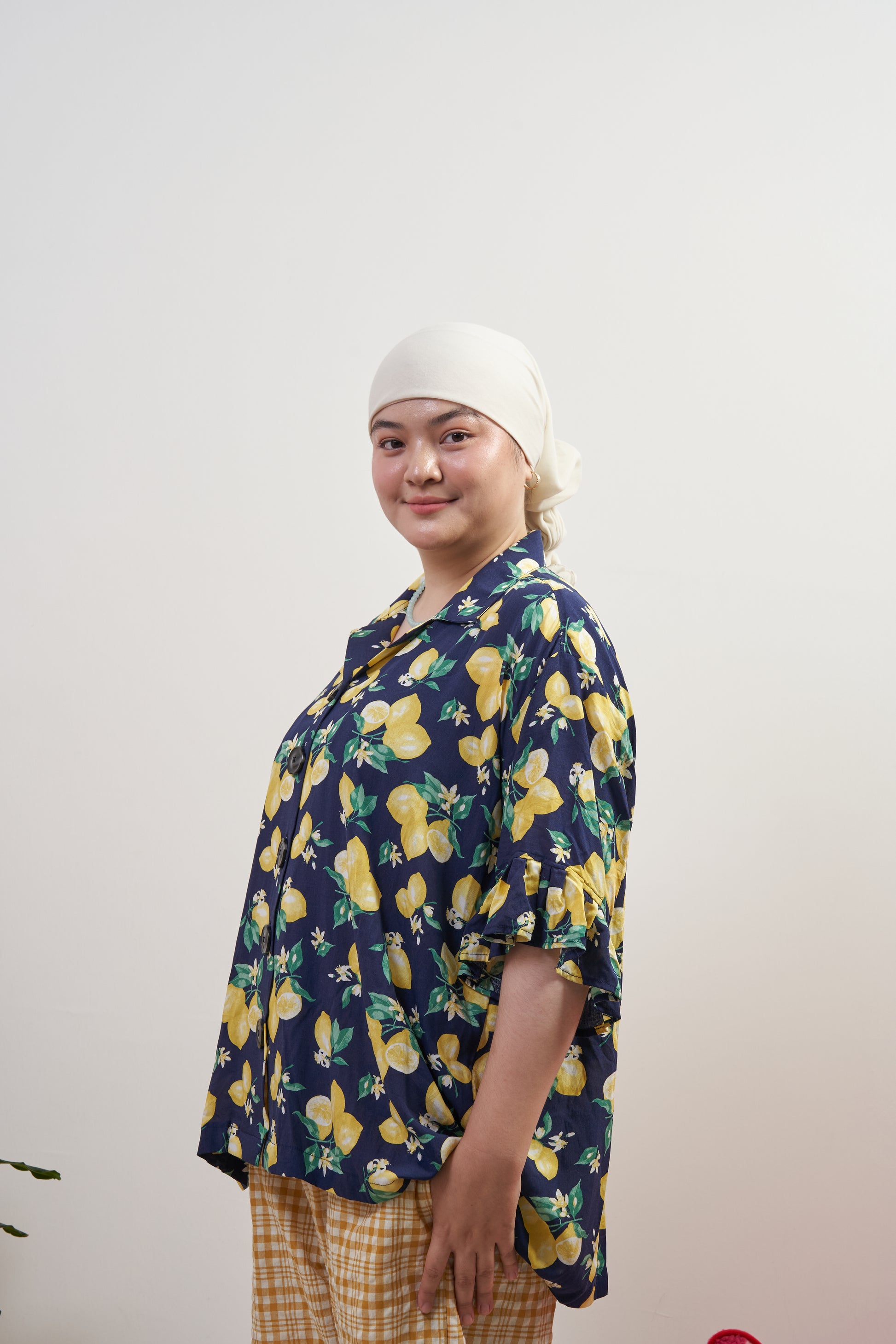Front side profile of Buttoned Belle Blouse in Lemon Dream, with one hand in pocket of Flutter Flair Pants in Lemonade, highlighting ruffled sleeve and lemon print.