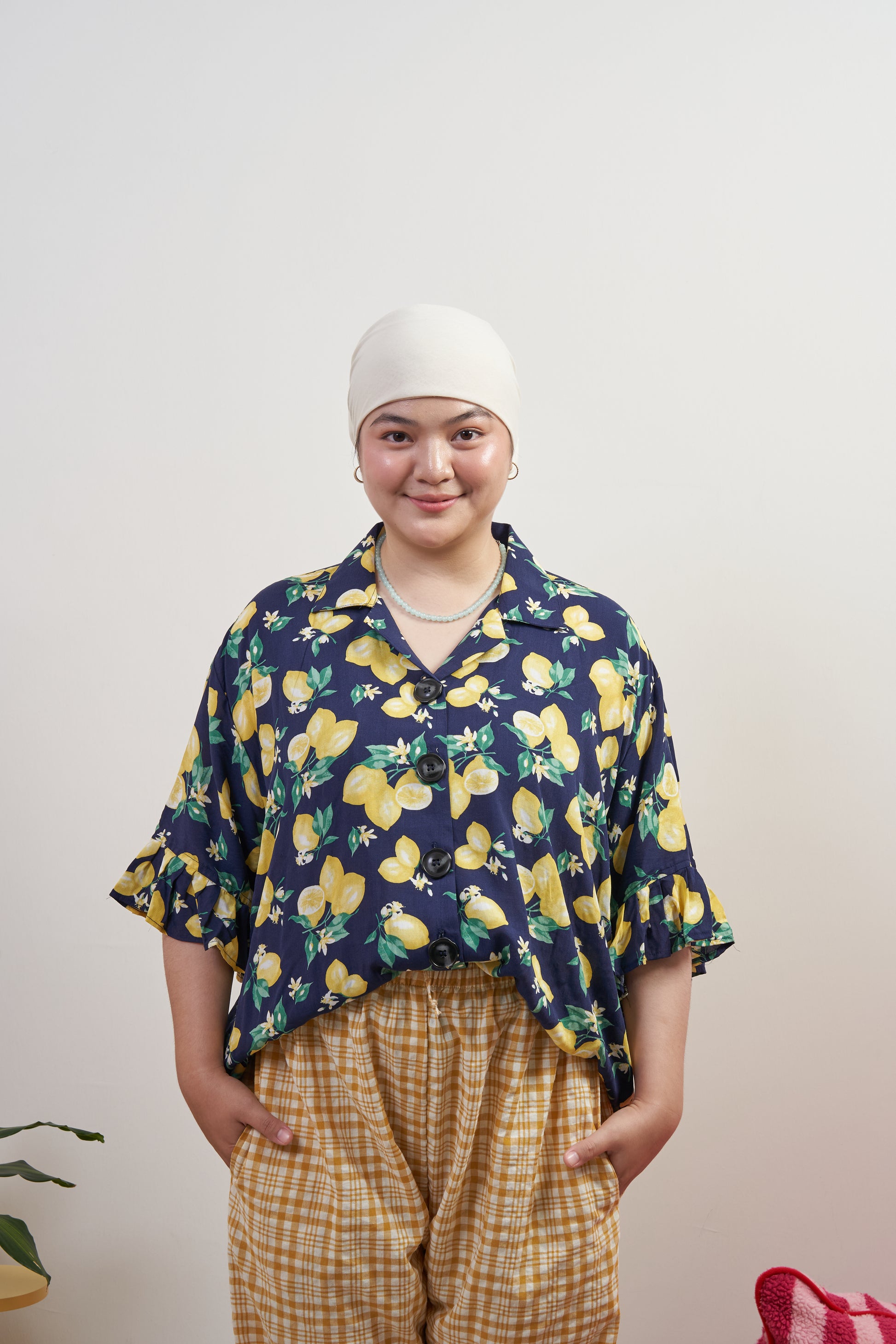 Model smiling in Buttoned Belle Blouse in Lemon Dream, styled tucked in with Flutter Flair Pants in Lemonade, showing vintage buttons, ruffled sleeves, and lemon print.