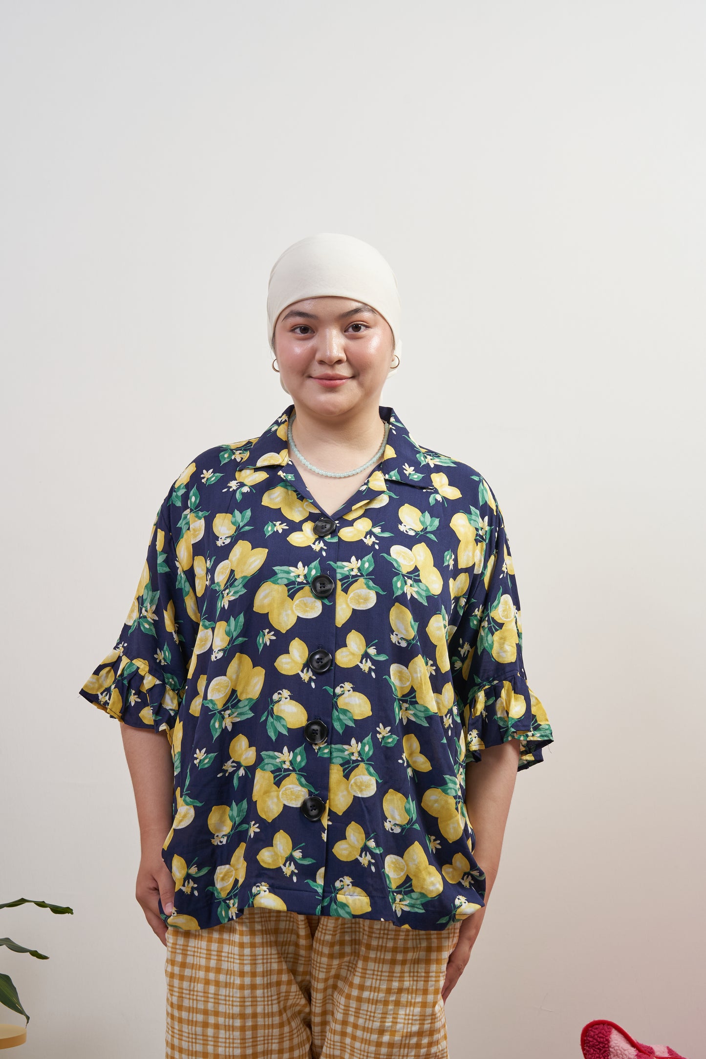 Model smiling and relaxed in Buttoned Belle Blouse in Lemon Dream, showing vintage buttons and ruffled sleeves against a dark blue base with lemon print.
