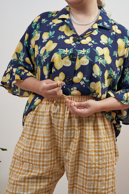 Close-up of Flutter Flair Pants in Lemonade, model tying the adjustable drawstring waist with Buttoned Belle Blouse in Lemon Dream tucked in.