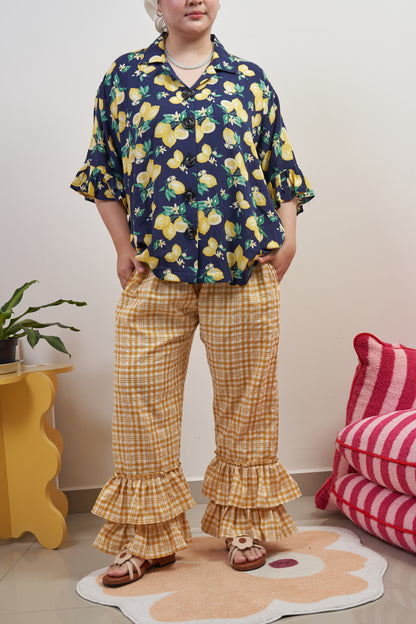 Front view of Flutter Flair Pants in Lemonade, model in relaxed stance with hands in pockets, highlighting double ruffles at the hem and loose fit