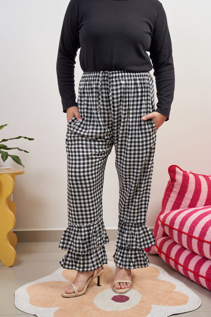 Front view of Flutter Flair Pants in Noir Blanc, highlighting black & white gingham pattern, double ruffles at the hem, drawstring waist, and loose fit with side pockets