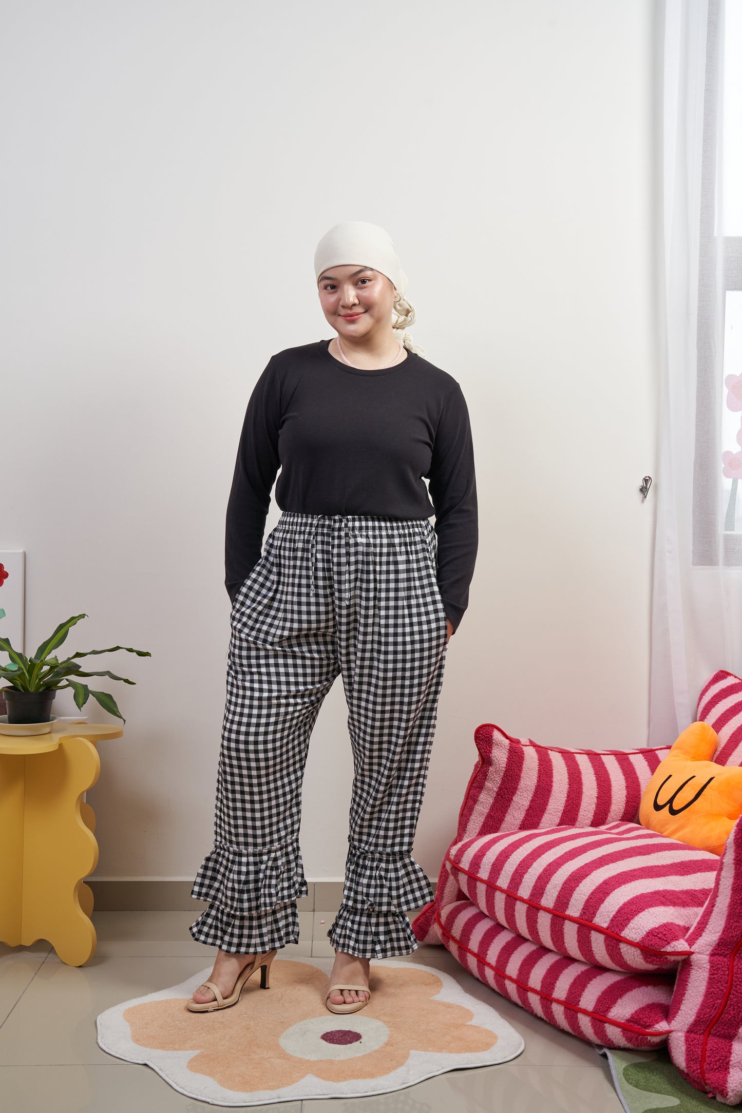 Full frontal view of Flutter Flair Pants in Noir Blanc, model with both hands in pockets, highlighting black & white gingham, double ruffle hem, drawstring waist, and loose fit.