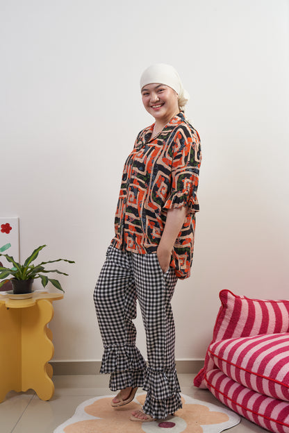 Side-front profile of Flutter Flair Pants in Noir Blanc styled with Buttoned Belle Blouse in Abstract Garden, untucked to show double ruffle hem, gingham pattern, and relaxed fit.