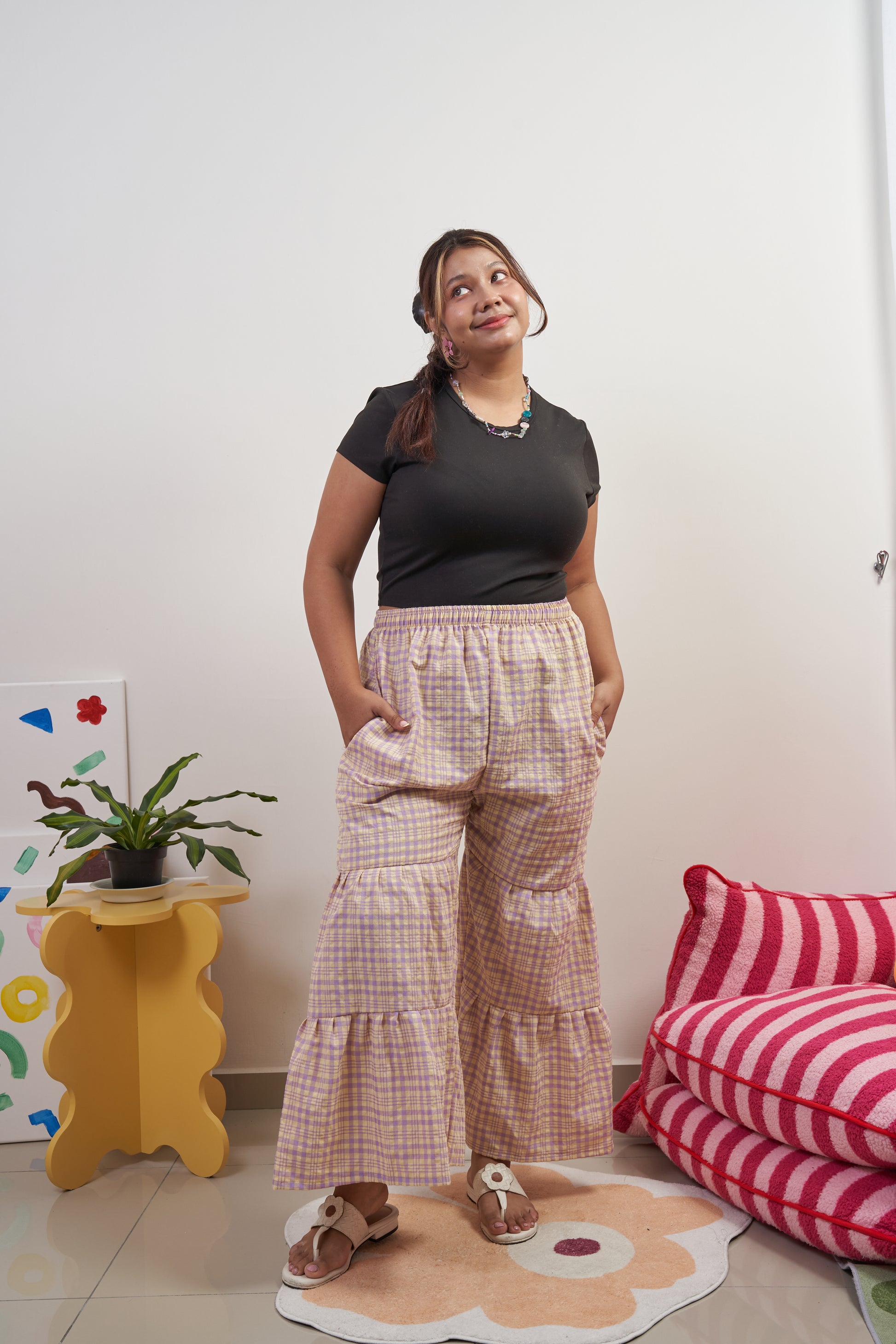 Front profile of Flutter Tier Pants in Orchid Zest, model with one leg extended forward to showcase breathability, purple and yellow plaid pattern, and double-tier ruffled flared hem