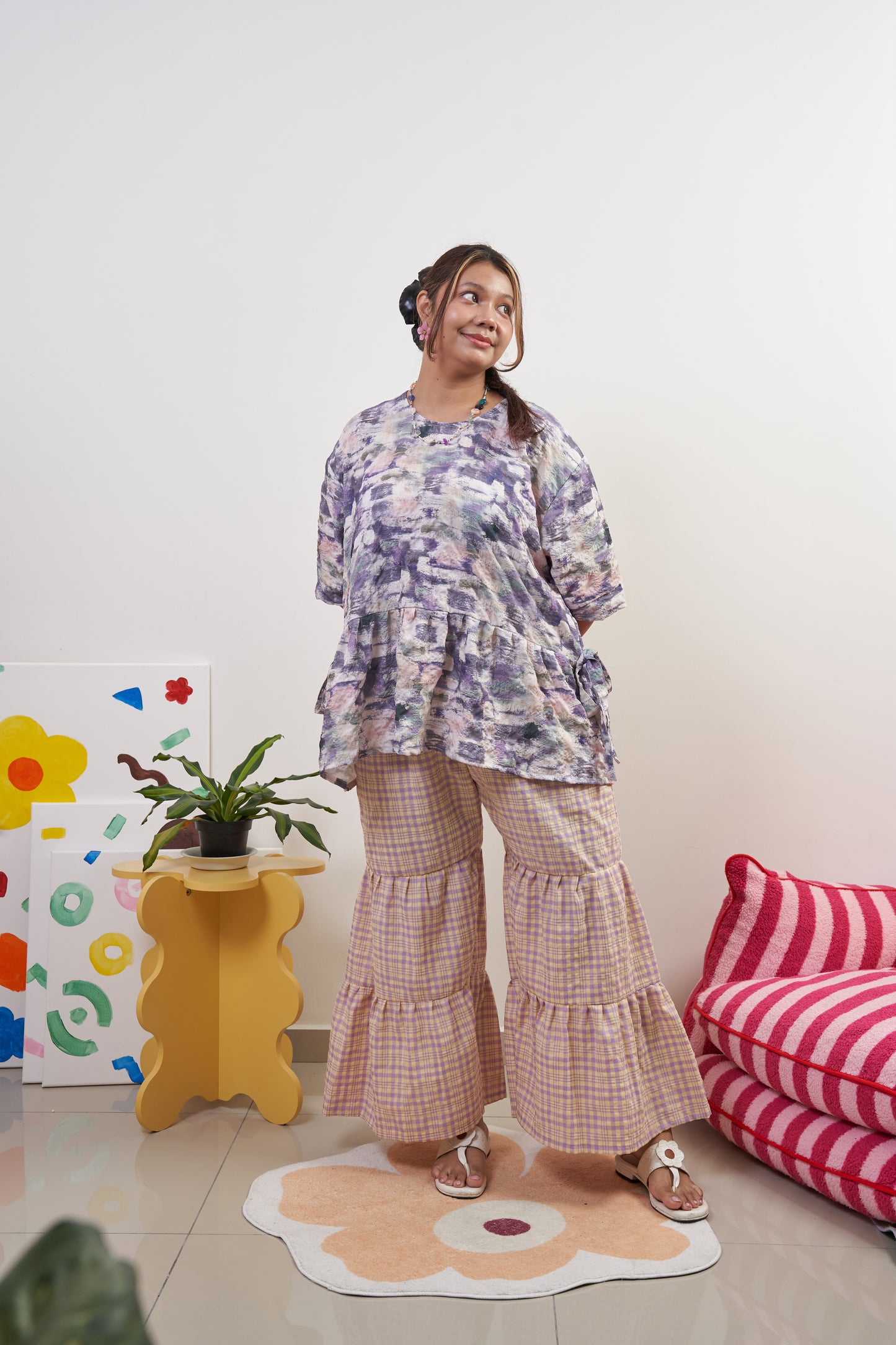 Full-body front view of Liliana Top in Wisteria with ribbon tied at side, styled with Flutter Tier Pants in Orchid Zest, showcasing purple peplum style and flared ruffle pants.
