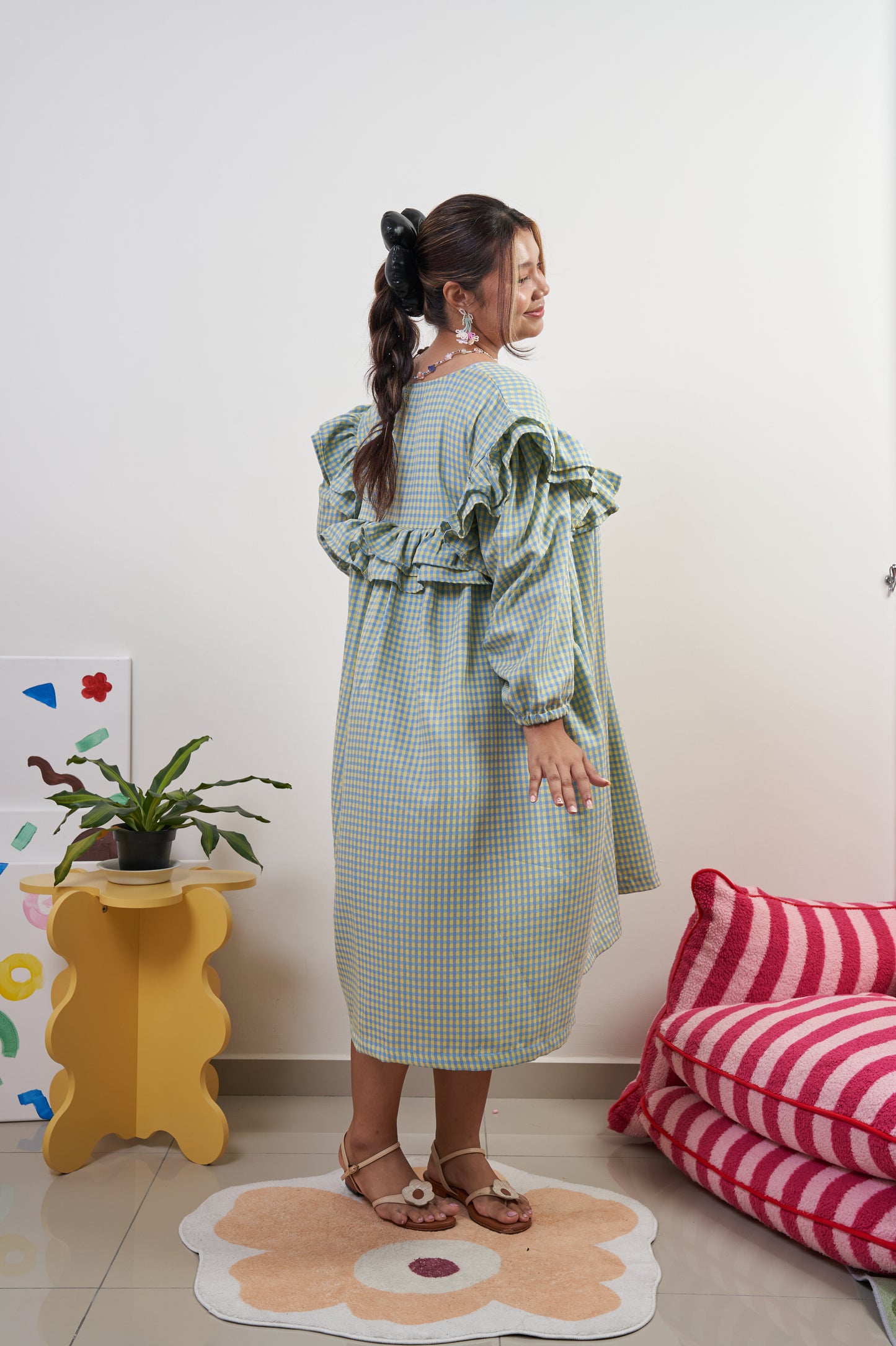 Back-side view of Rhea Dress in Felicia Daisy, showcasing the yellow and blue gingham print, ruffles, and flowing tent dress silhouette