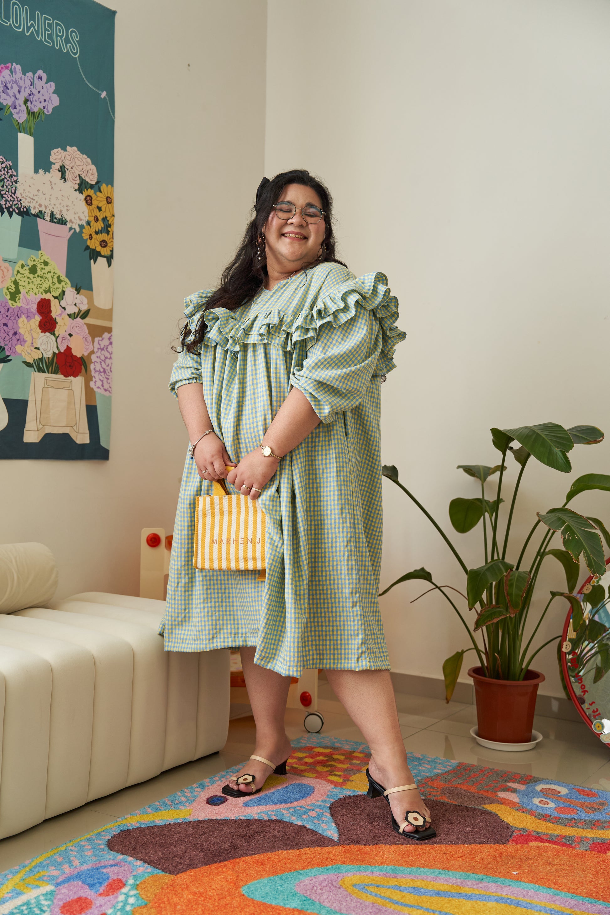 Semi-side frontal view of Rhea Dress in Felicia Daisy, featuring yellow and blue gingham print with a flowing tent dress silhouette and ruffles