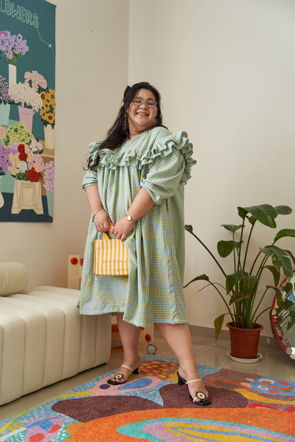 Semi-side frontal view of Rhea Dress in Felicia Daisy, featuring yellow and blue gingham print with a flowing tent dress silhouette and ruffles