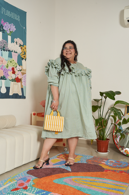 Semi-side frontal view of Rhea Dress in Felicia Daisy, model in a slightly different pose, showcasing the flowing gingham print and ruffles