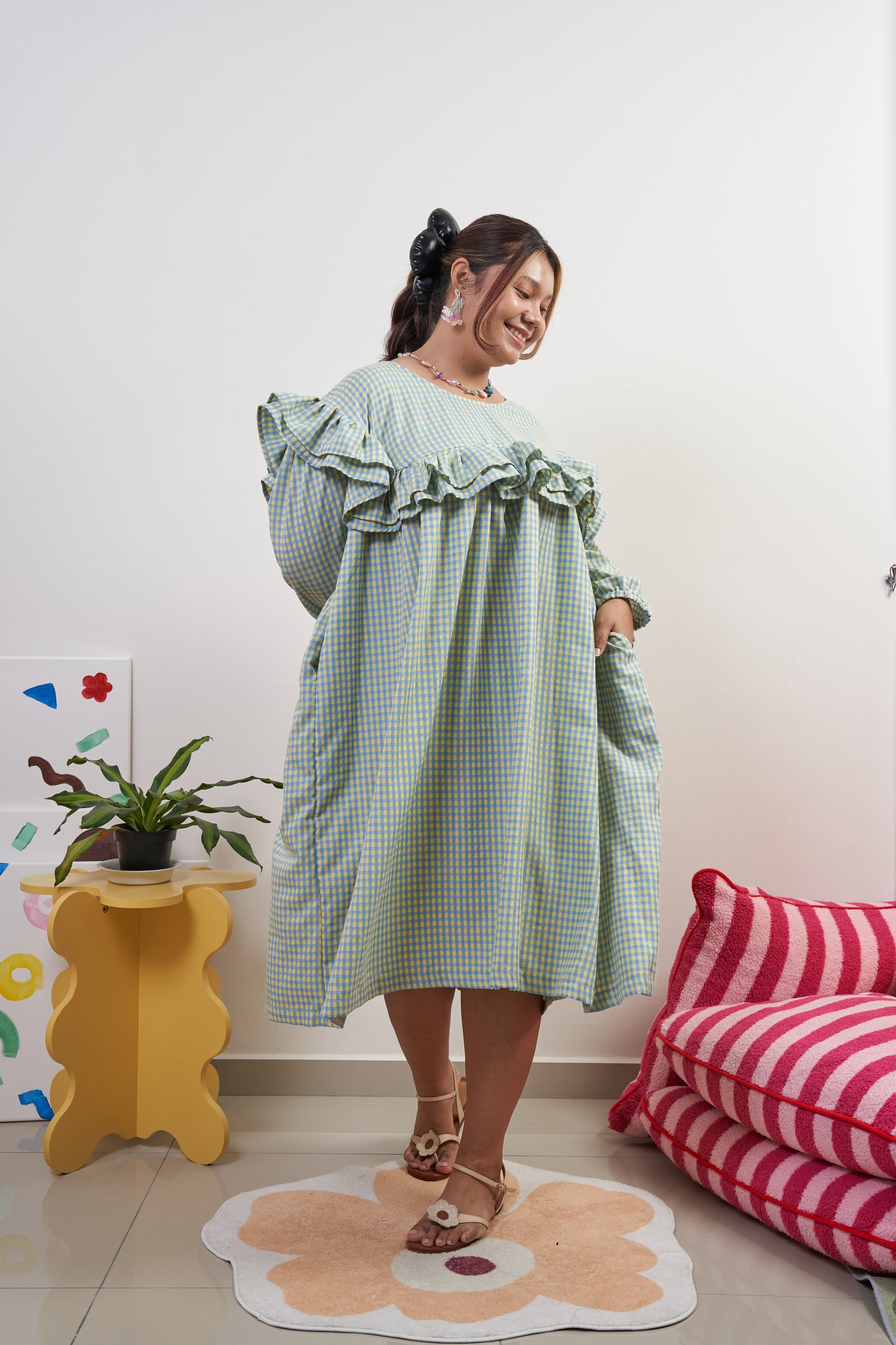 Rhea dress in Felicia Daisy, yellow and blue gingham print, with model twirling to show the flowing trapeze silhouette and ruffles